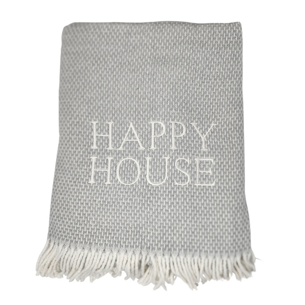 The Happy House Throw by A Soft Idea is a folded, light gray woven throw with white fringe and "HAPPY HOUSE" embroidered in large white letters; exclusive for home, and machine washable for easy care.