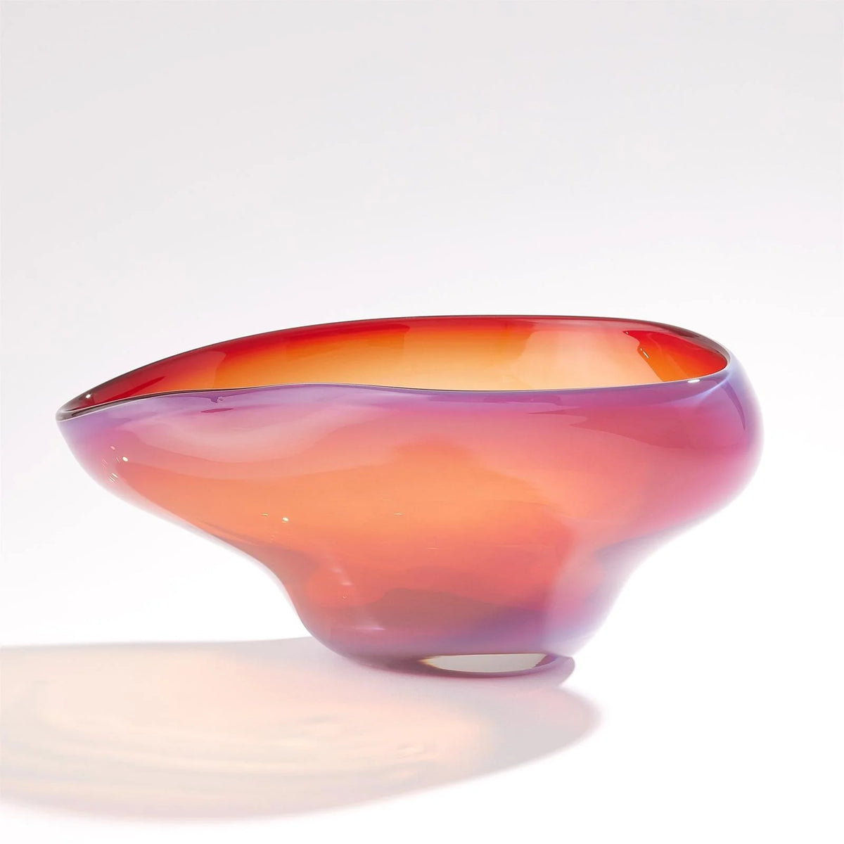 The Harmony Bowl Red - Small by Global Views / Surya is an asymmetrical, handmade piece crafted from handblown art glass, showcasing a smooth and flowing silhouette with gradient hues transitioning from deep pink to orange—a striking example of modern luxury décor set against a plain white background.
