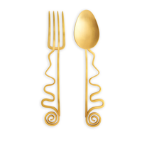 The Spirale Gold Serving Set by L'Objet includes a fork and spoon with wavy, spiral-ended handles, beautifully displayed side by side—ideal for gifting in a luxury box.
