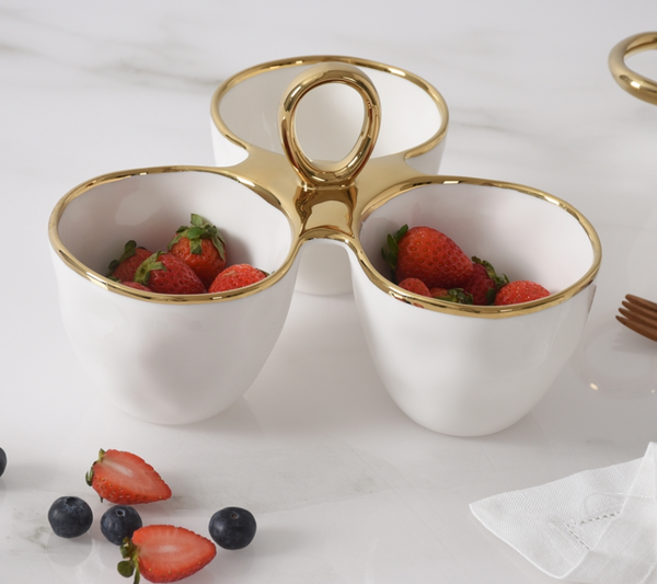 The PAMPA BAY Golden Handle 3 Section Server, crafted from white porcelain with a gold rim, features three sections filled with fresh strawberries. Blueberries and sliced strawberries are scattered on the marble surface nearby.