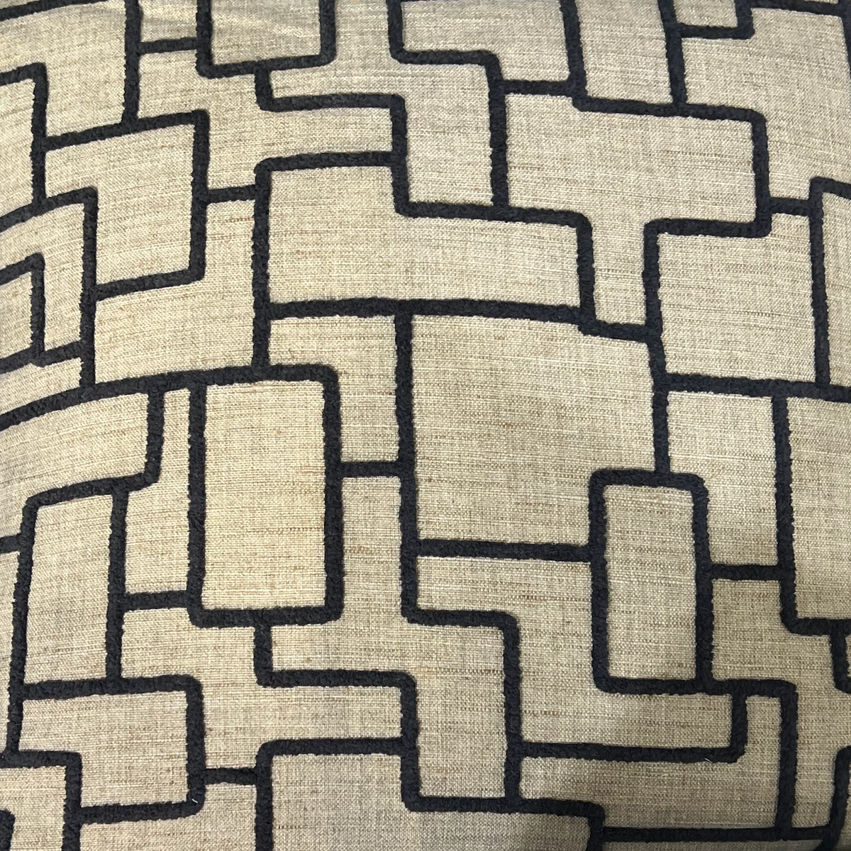 A close-up of Decor Fifty-Five’s Shapeshifter Pillow Black & Tan shows its beige fabric with interlocking, irregular rectangles in dark thread, creating a maze-like contemporary pattern.