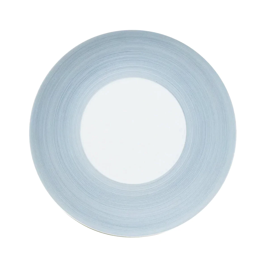 A round, white plate from the JL Coquet Hemisphere Dinnerware Storm Blue collection with a wide, storm blue rim featuring subtle circular lines, viewed from above on a plain white background.