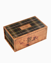 A wooden box with an heirloom-quality finish and faux wood-grain detail features the Oh My Mahjong logo on the side and “Heritage” on its tartan-patterned lid. Designed to store your Mahjong Tiles Set - Heritage by Oh My Mahjong, the closed box is photographed against a white background.