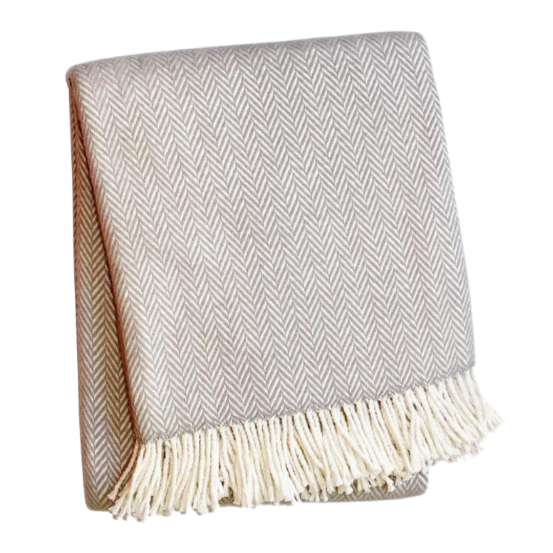 A Soft Idea's Herringbone Plush Throw in beige, with a subtle herringbone pattern and white fringed tassels along one edge, is folded against a plain white background. This cozy blanket is perfect for any space.