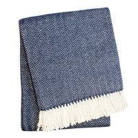 The Herringbone Plush Throw by A Soft Idea features a folded navy blue and white herringbone pattern with white fringe, is soft to the touch, machine washable, and shown against a white background.