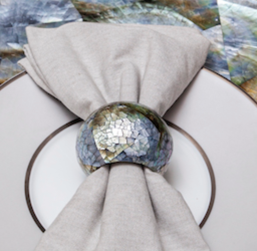 A cloth napkin is held by a Von Gern Home Shell Pearl Black Napkin Ring, set of 4, displayed on a white plate with a silver rim.