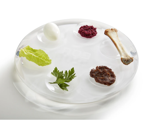 The Apeloig Acrylic Seder Plate features a modern design and holds a hard-boiled egg, red beet paste, a bone, romaine lettuce, parsley, and brown paste—beautifully representing Passover traditions.