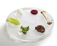 The Apeloig Acrylic Seder Plate features a modern design and holds a hard-boiled egg, red beet paste, a bone, romaine lettuce, parsley, and brown paste—beautifully representing Passover traditions.