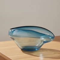 A modern, asymmetrical Harmony Bowl Dark Blue from Global Views / Surya with an ombré design rests on a light wooden surface, casting a gentle shadow in natural daylight. This distinctive serving piece brings sophistication to any setting.