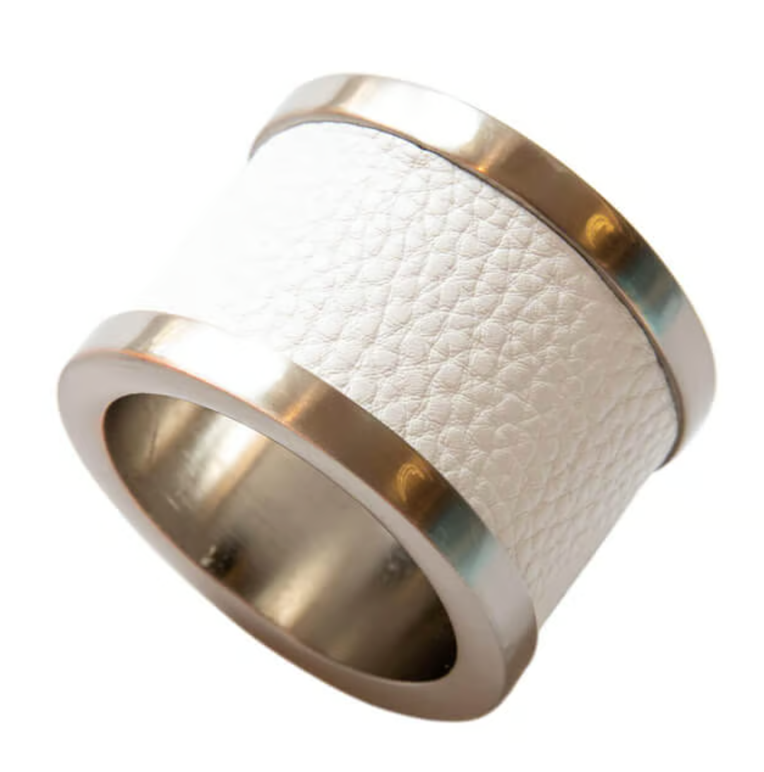 The Von Gern Home Zinc & Leather Napkin Ring S/4 features a wide metallic design with shiny gold edges and a textured white leather center, displayed against a white background.