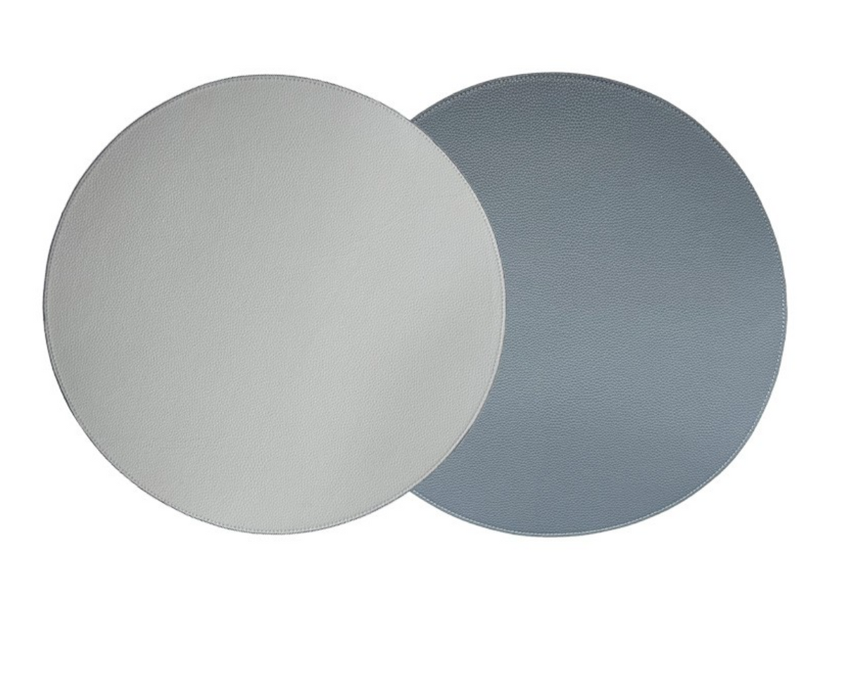 Two circular, reversible placemats from Von Gern Home (set of 4) overlap; the left is light gray, the right medium blue-gray. Each features subtle texture, ideal for an elegant table setting against a white background.
