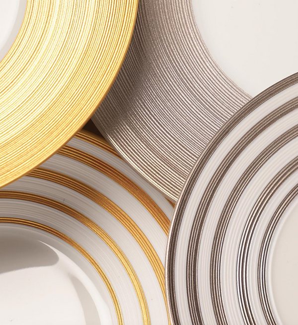 Four overlapping JL Coquet Hemisphere Dinnerware plates in Grey Stripes display metallic gold and silver rims, highlighting their circular patterns and glossy porcelain texture in a close-up view.