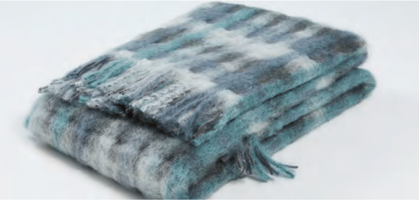 A folded, fuzzy Mia Throw by Mantas Ezcaray features a blue, gray, and white plaid pattern with fringed edges and artisanal quality, displayed on a plain light background.