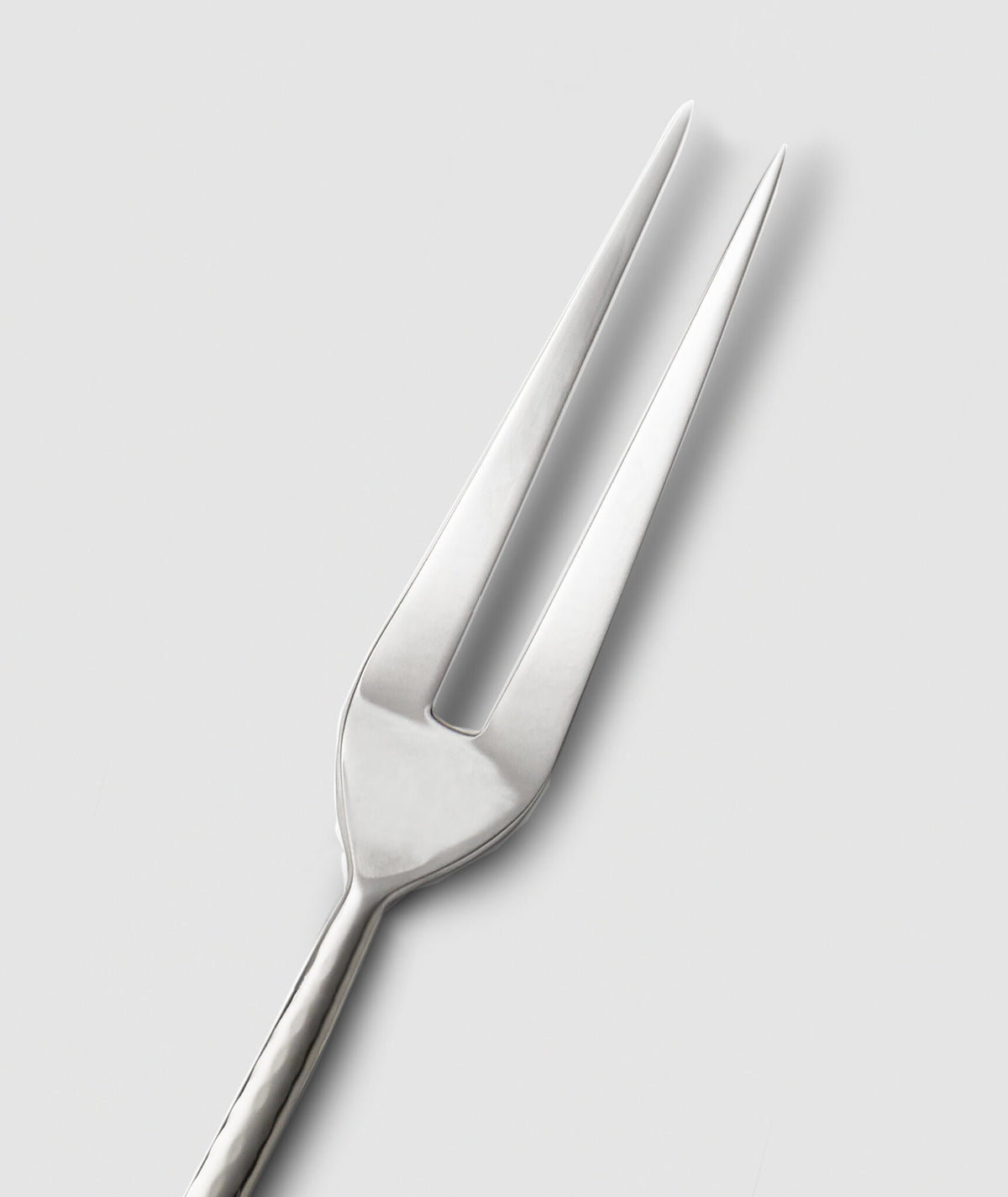 The Mary Jurek Alta Meat Serving Fork, with its two long, pointed tines, is set diagonally on a plain light gray background—an elegant stainless steel addition to your serving utensils.