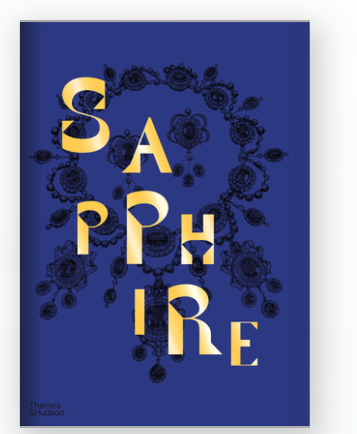 A book cover with a deep blue background features "Sapphire: A Celebration of Color" in bold gold letters over ornate black jewelry art, capturing the gem’s allure. Joanna Hardy's name and the W.W. Norton Company logo appear below.