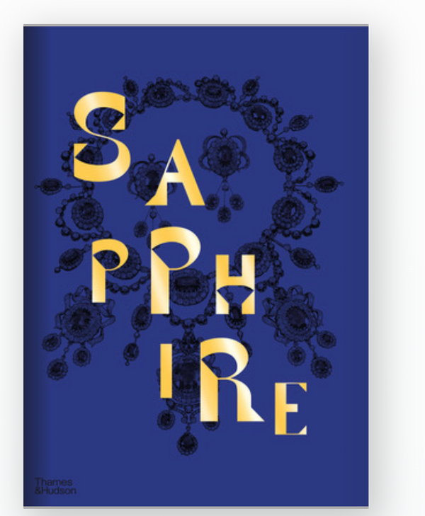 A book cover with a deep blue background features "Sapphire: A Celebration of Color" in bold gold letters over ornate black jewelry art, capturing the gem’s allure. Joanna Hardy's name and the W.W. Norton Company logo appear below.