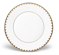 A round white plate from the Aegean Filet Gold Dinnerware by L'Objet, crafted in fine porcelain with a scalloped 24k gold border and a gold line near the center, shown on a plain white background.