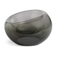 The Axiom Glass Caldera Vessel Medium 9" is a hand-blown, smoky gray glass centerpiece with a round shape and asymmetrical slanted opening, elegantly displayed on a white background.