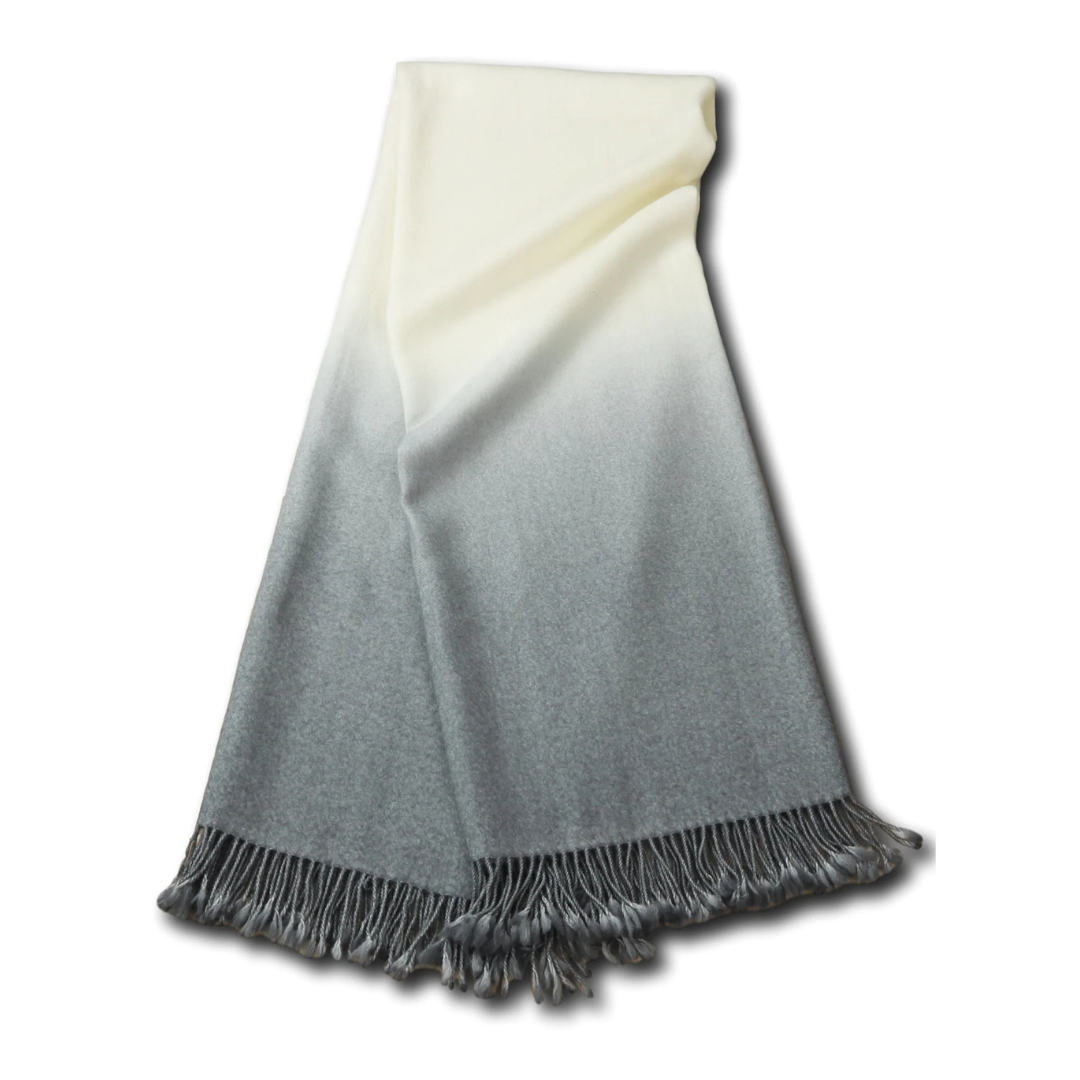 The Johanna Howard Dip Dye Throw features an ombré design fading from cream to gray, accented with fringed tassels. This cozy blanket adds style and comfort, beautifully displayed on a white background.