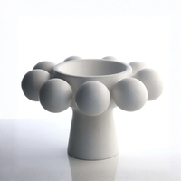 The KleinReid Nimbus Footed Bowl Alabaster features a wide opening and a ring of smooth, hand-appliquéd porcelain spheres around the rim, showcased against a bright, minimalist background.