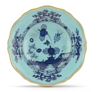 The Oriente Italiano Dinnerware Iris by Ginori 1735 features a scalloped edge with gold rim, a light blue background, and dark blue chinoiserie floral motifs at the center and border.