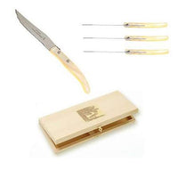 The Berlingot Steak Knives s/6 Assorted by Claude Dozorme are displayed on a white background, featuring six serrated steak knives with light handles and presented in a light wooden box adorned with a gold emblem.