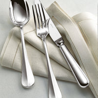 The Sambonet Baguette Stainless Steel 5PPS set—a spoon, fork, and knife—are elegantly placed on a cream cloth napkin atop a light fabric surface, highlighting the timeless style of this flatware.