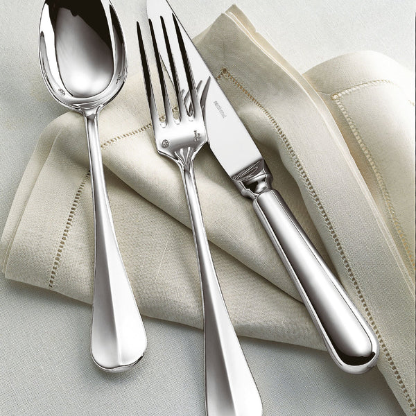 The Sambonet Baguette Stainless Steel 5PPS set—a spoon, fork, and knife—are elegantly placed on a cream cloth napkin atop a light fabric surface, highlighting the timeless style of this flatware.