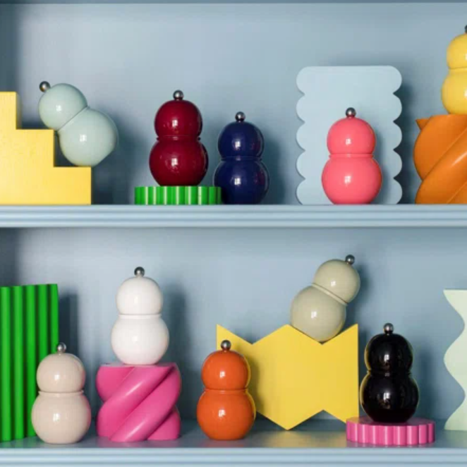 Addison Ross Chubbie Bobbin Salt or Pepper Shakers with high-gloss lacquer in green, yellow, blue, and pink stand out among geometric decor on shelves against a light blue background.