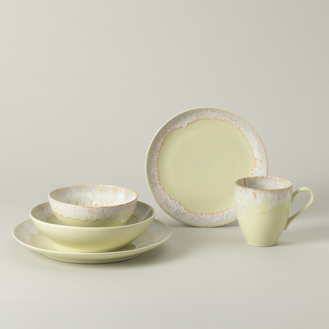 The Costa Nova Taoromina Dinnerware Yellow is a five-piece pale yellow stoneware set with a glossy, textured rim and soft white and tan accents. Includes mug, bowl, salad plate, dinner plate, and pasta bowl arranged on a neutral background.