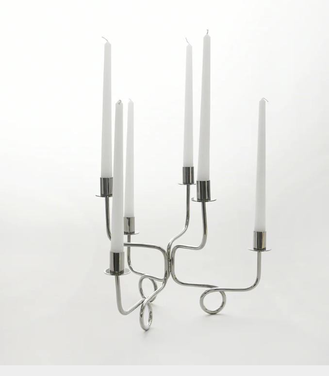 The Together Candelabra - Silver by Byaas, featuring a geometric looped base and minimalist design, displays six tall white taper candles against a plain white background.