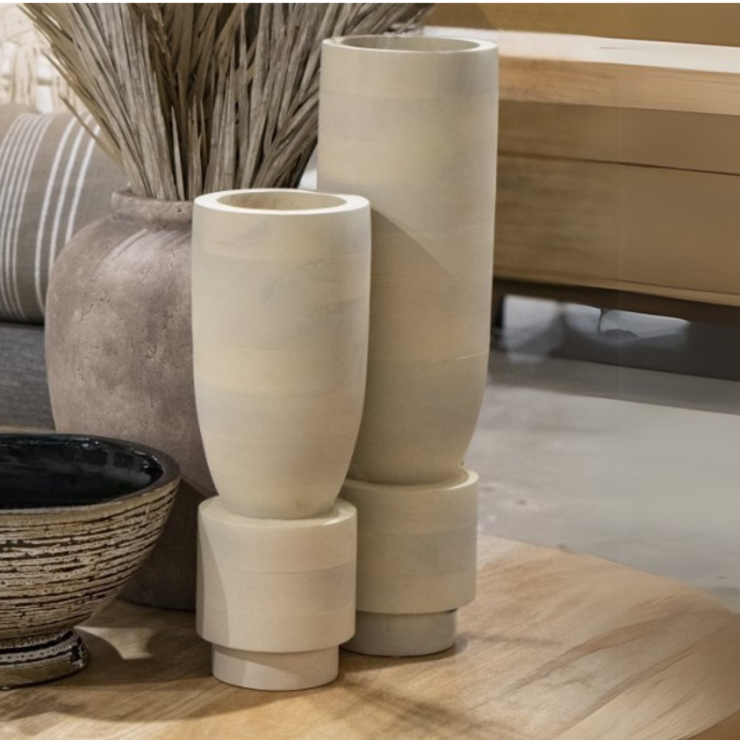 Two tall Bastone Vases by Elk Group with geometric bases sit on a wooden table next to a textured brown pot of dried grass and a black ceramic bowl in a cozy, contemporary living space.