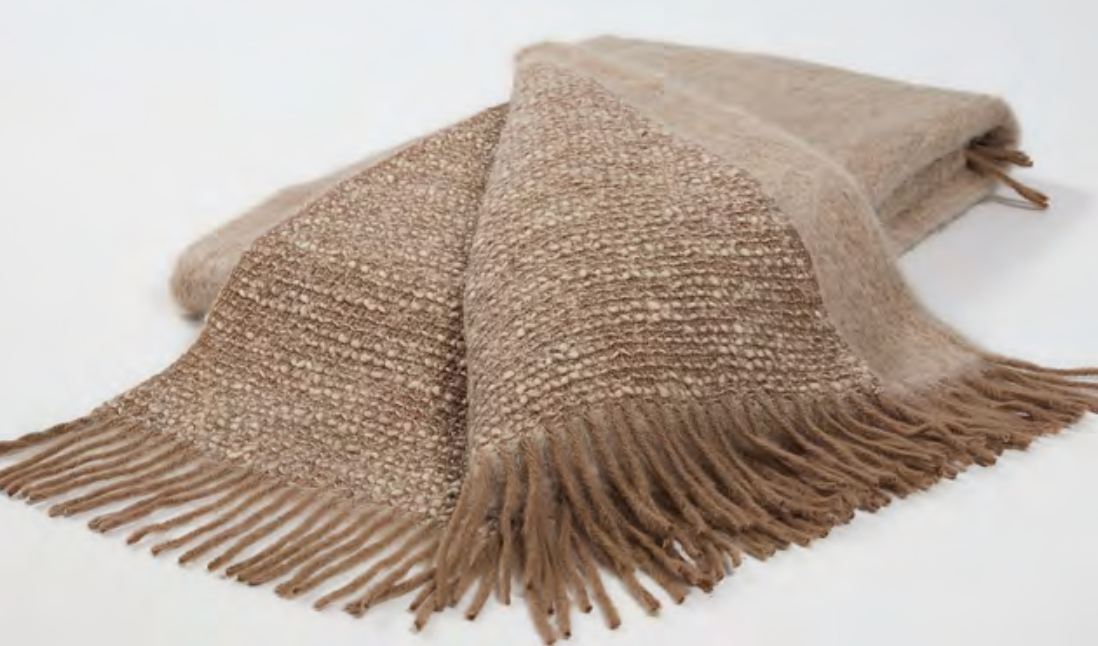 The Coco Throw by Mantas Ezcaray is a luxurious double-sided blanket in beige and brown Chanel fabric, featuring fringed edges and elegantly displayed on a white background.