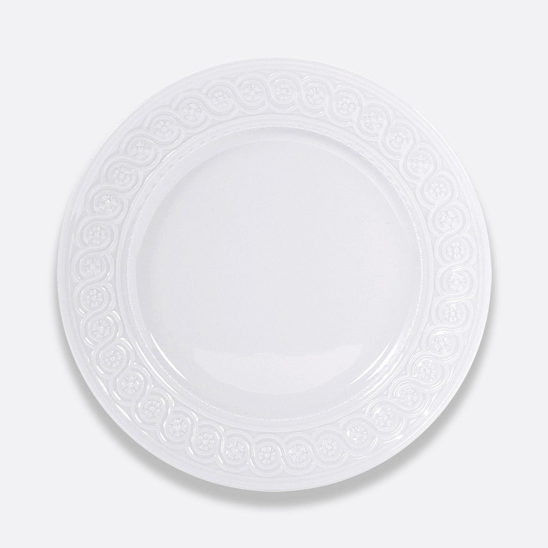 The Louvre Dinnerware by Bernardaud is a round, white ceramic plate featuring an ornate, Renaissance-inspired embossed border, showcased against a plain light gray background.