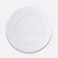 The Louvre Dinnerware by Bernardaud is a round, white ceramic plate featuring an ornate, Renaissance-inspired embossed border, showcased against a plain light gray background.