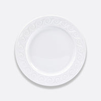 The Louvre Dinnerware by Bernardaud is a plain white ceramic plate featuring a decorative swirl pattern inspired by Renaissance French architecture, shown from above on a light gray background.