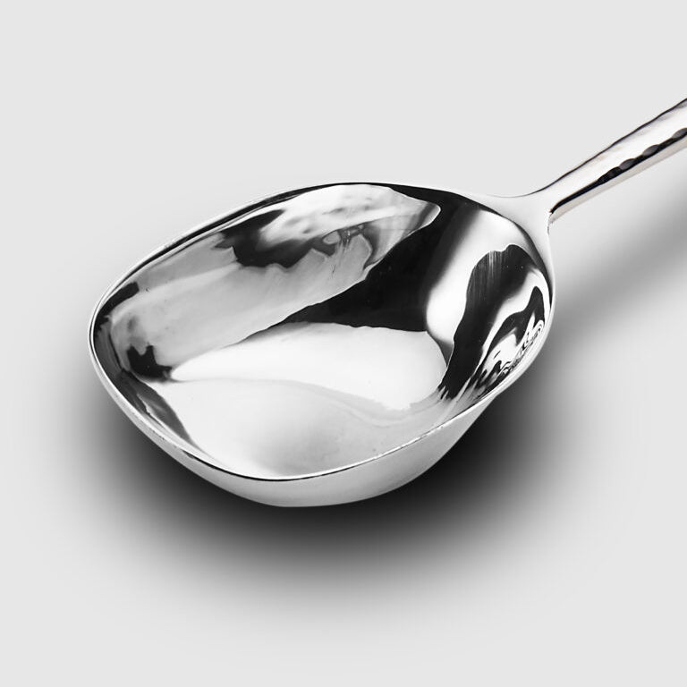 A close-up of the Mary Jurek Alta Deep Garden Vegetable Spoon showcases its shiny stainless steel and smooth, curved surface on a plain light gray background.