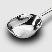 A close-up of the Mary Jurek Alta Deep Garden Vegetable Spoon showcases its shiny stainless steel and smooth, curved surface on a plain light gray background.