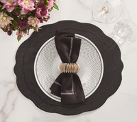 A black scalloped placemat with a matching plate, topped with Kim Seybert's Classic Napkin - Earthtones Set of 4, held by a gold napkin ring. Pink flowers to the left and two clear glasses on marble complete this elegant table decor.