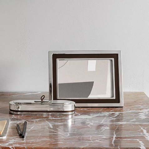 A Georg Jensen Manhattan Picture Frame and a stainless steel-lidded glass container rest on brown marble with a pen, notepad, and a plain light wall in the background.