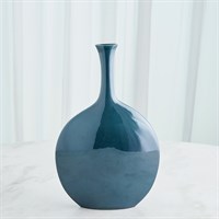 The Silhouette Reactive Vase Blue by Global Views/Surya, a Portuguese ceramic vase with a glossy deep blue glaze, round body, and long narrow neck, sits on a light surface before sheer white curtains.