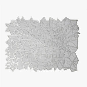 The Geometric Challah Cover by Apeloig is a modern white cover with an abstract pattern of polygons and triangles, featuring Hebrew text on the lower right.