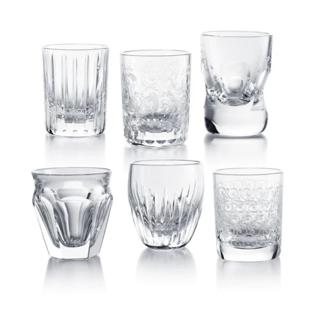The Baccarat Take A Shot - Les Mini Set features six elegant glass tumblers, each with a distinct etched or molded design and unique shape, arranged in two rows on a white background for a stylish display.