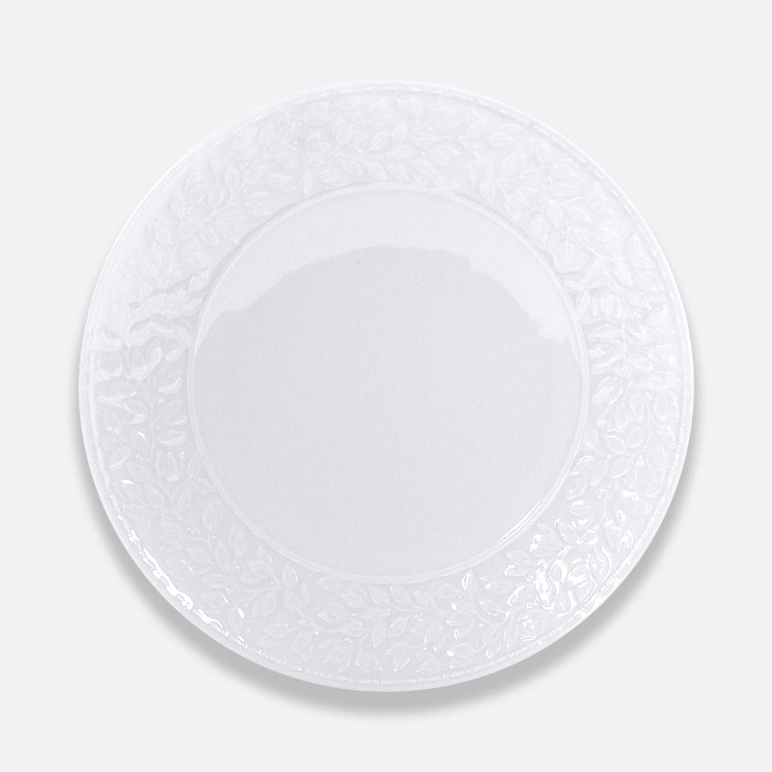The Bernardaud Louvre Dinnerware features a plain white ceramic plate with a subtle embossed floral rim, inspired by Renaissance white service, shown from above on a light gray background.