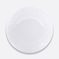 The Bernardaud Louvre Dinnerware features a plain white ceramic plate with a subtle embossed floral rim, inspired by Renaissance white service, shown from above on a light gray background.