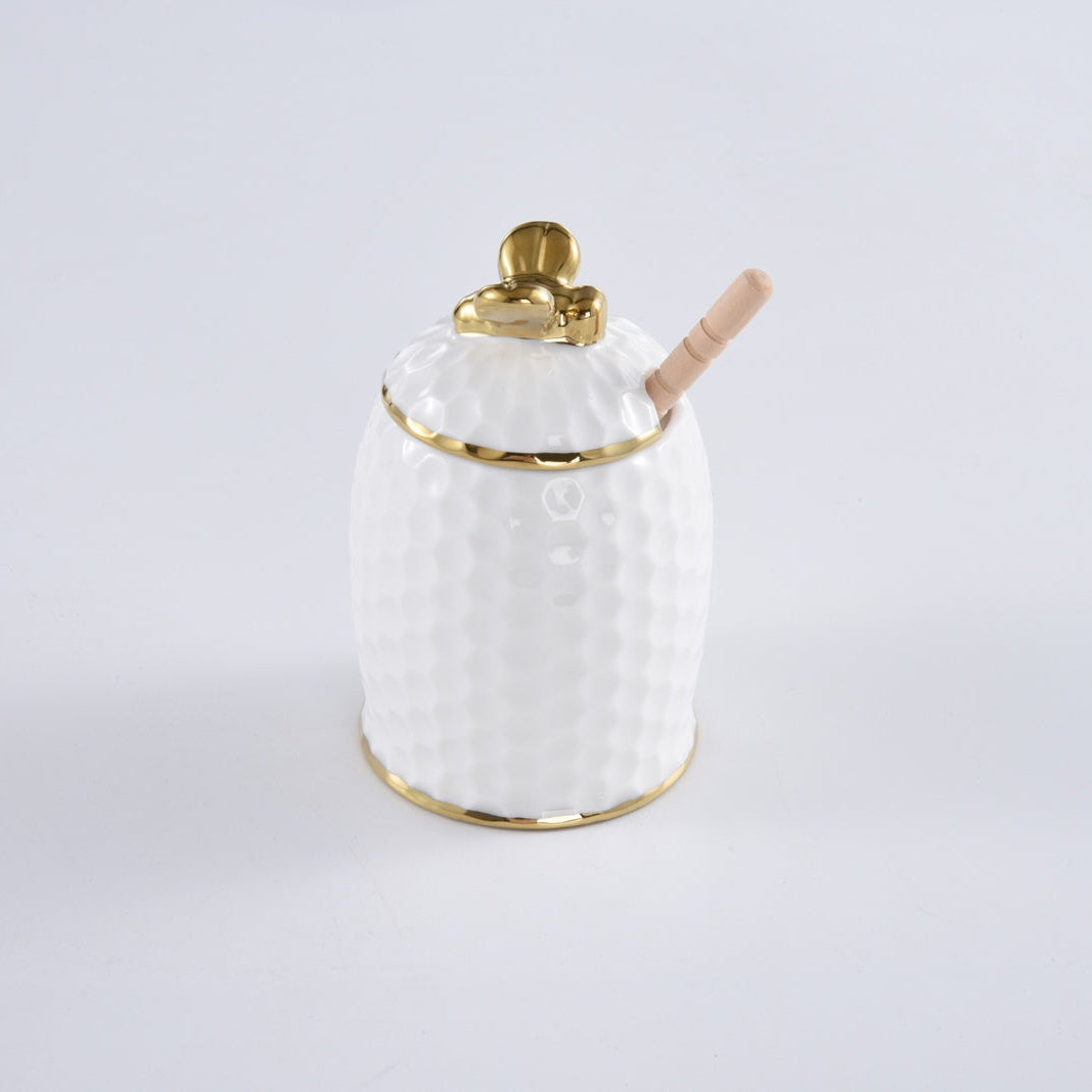 Introducing the PAMPA BAY Honey Jar Set: a white textured porcelain honey jar adorned with a gold trim and topped with a golden honeybee. This elegant set includes a wooden honey dipper, making it the perfect hostess gift sure to delight.