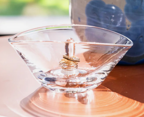 Gold wedding rings are stacked on the Simon Pearce Champlain Ring Holder, displayed in a clear glass dish.