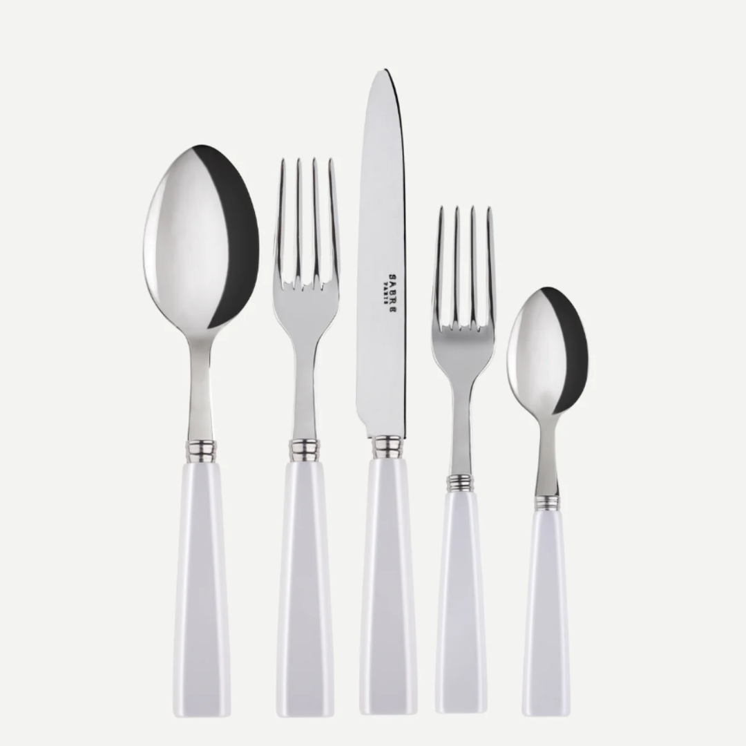 The Sabre Icone 5pps w/ Serrated Knife by Sabre features five stainless steel utensils with white handles—tablespoon, serrated dinner knife, dinner fork, salad fork, and teaspoon—arranged side by side on a white background; all are dishwasher safe.