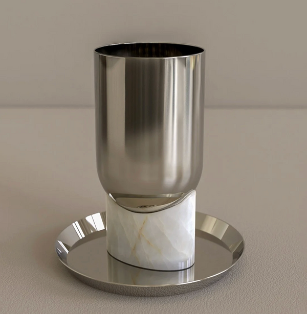 The Onyx Kiddush Cup by CDMX / BRUCI features a silver cup with a marble-like white onyx base, displayed on a shiny round tray against a plain beige background.