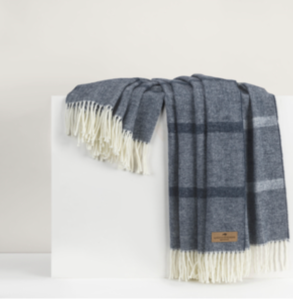 A folded dark gray and blue Montauk Stripe Throw by Lands Downunder, featuring white fringe, is draped over a white rectangular surface against a neutral background.